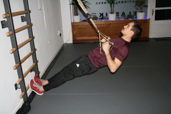 Row HIIT Übung Trainer führt einen Row mit einem Schlingentrainer aus